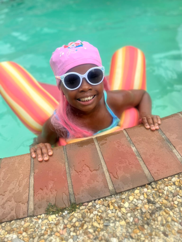 Girl in pool on rainbow float wearing SwimHair cap and sunglasses